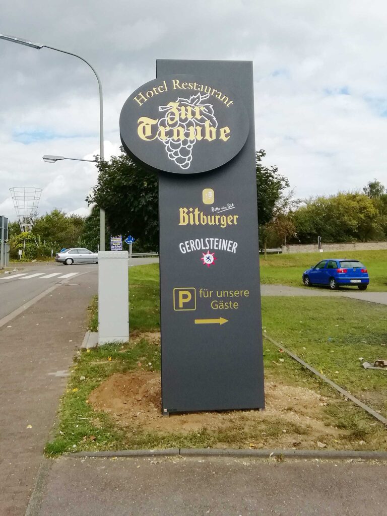 beleuchtete Pylone Hotel Restaurant Traube mit Bitburger- und Gerolsteiner-Werbung in grau mit weißer und goldfarbener Beschriftung